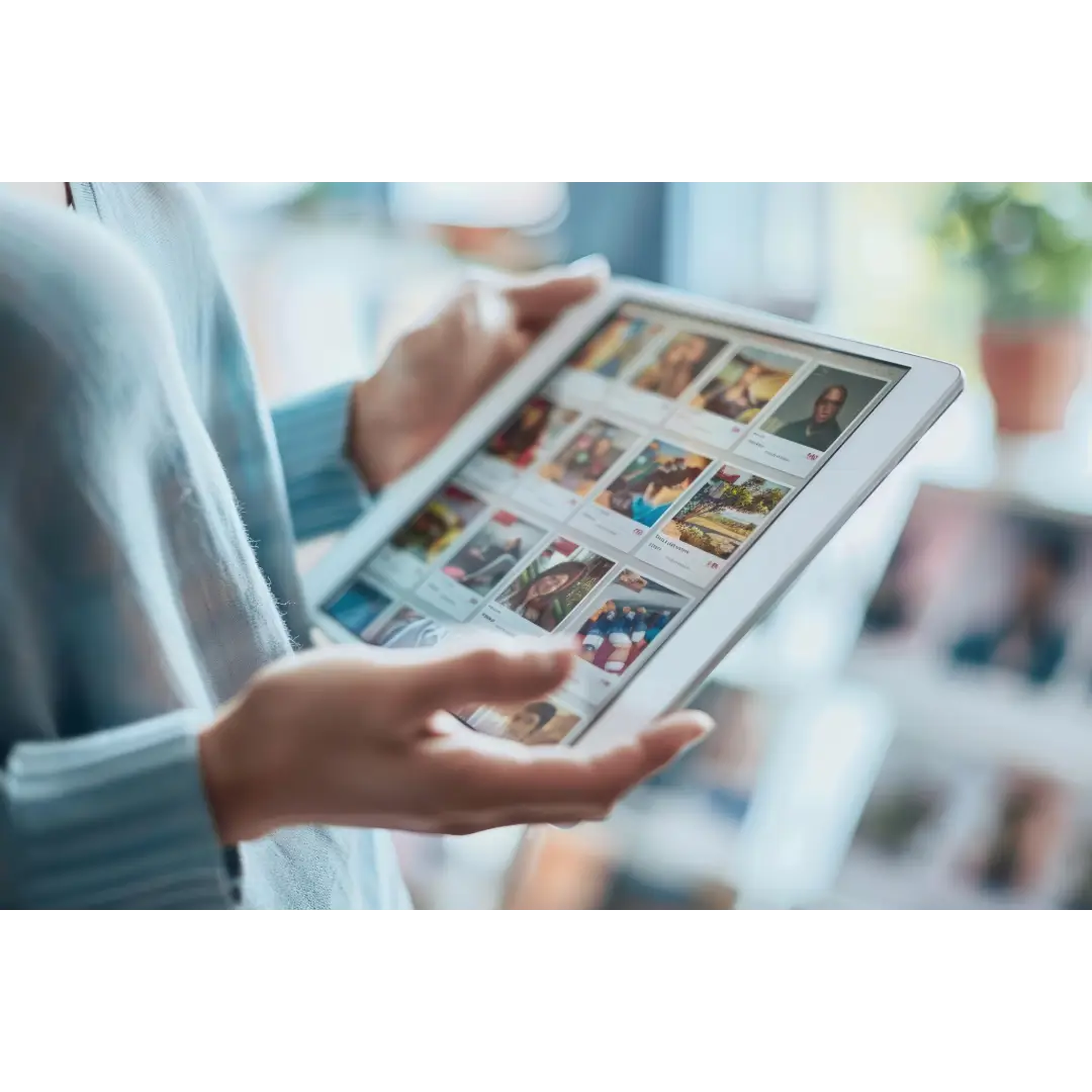 Person holding a tablet browsing photos in a bright room.